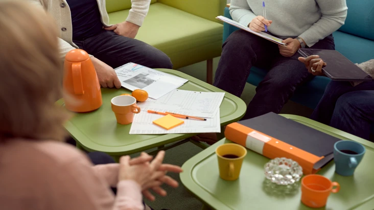 Ett bord fullt med papper och kaffekoppar och man ser att flera samtalar med varann.