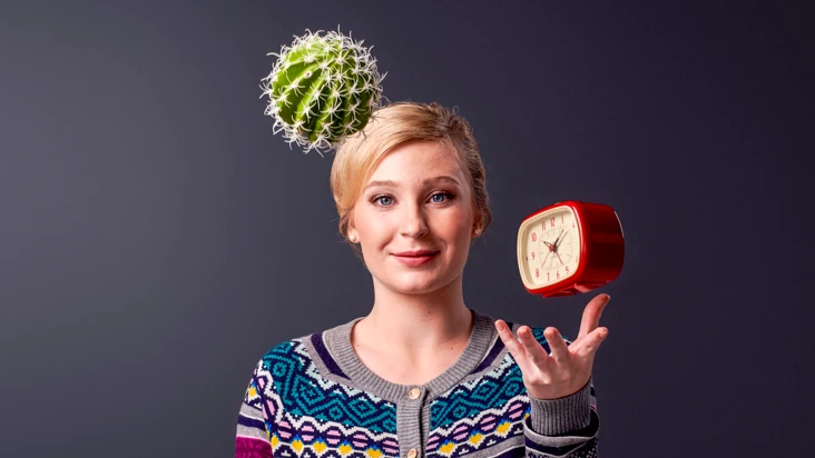 En kvinna jonglerar med en kaktus och en väckarklocka.